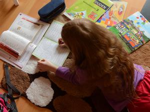 Ein achtjähriges Mädchen liegt auf einem Teppich in ihrem Kinderzimmer und erledigt Hausaufgaben im Fach Deutsch.