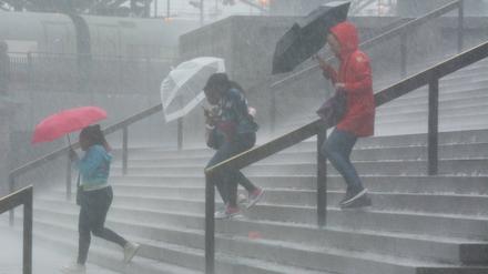 Vor dem Kölner Hauptbahnhof kämpfen Menschen mit starken Regenfällen.