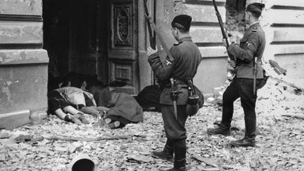 Niederschlagung des Aufstandes im Warschauer Ghetto (1943): Zwei Soldaten  „fremdvölkischer Hilfseinheiten“ der SS stehen vor den Leichen getöteter Juden in einem Hauseingang.