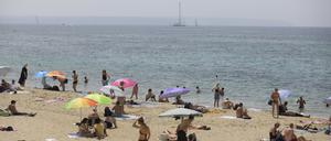 08.07.2023, Spanien, Palma: Menschen sonnen sich und benutzen Sonnenschirme am Strand Can Pere Antoni in Palma während der Hitzewelle.