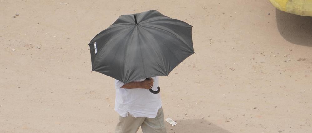Bangladesch, Naogaon: Ein Mann schützt sich inmitten einer Hitzewelle mit einem Regenschirm vor Sonnenstrahlen.