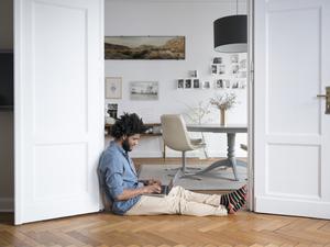 Ein Mann sitzt zu Hause auf dem Boden, mit einem Laptop in seinem Schoß.