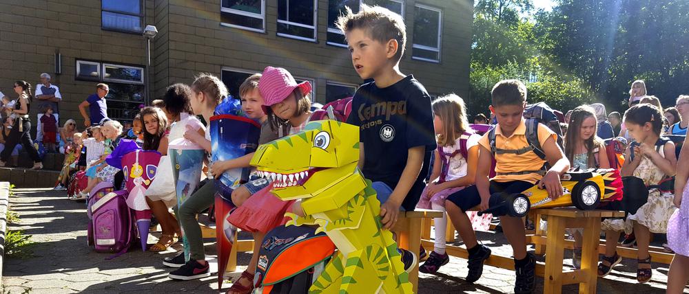 Kinder bei der Einschulung mit Ihren Schultüten auf dem Schulhof, im Vordergrund ein Kind mit Dinosaurier-Schultuete.