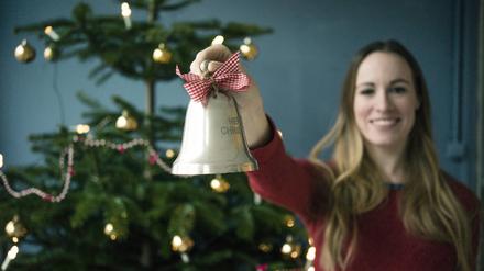 Eine lächelnde Frau zeigt eine Weihnachtsglocke.