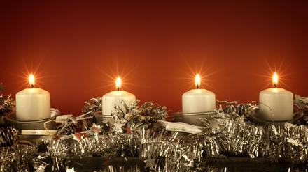 Adventsdekoration mit vier brennenden Kerzen vor rotem Hintergrund.