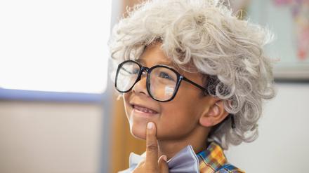 Thoughtful schoolboy wearing wig in classroom.