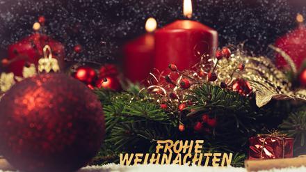 Adventskranz mit brennender Kerze und einer Holzschrift: Frohe Weihnachten.