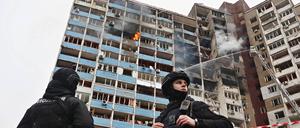 Zwei Sicherheitsbeamte stehen vor einem brennenden Hochhaus in Kiew, das von russischen Luftangriffen getroffen wurde.