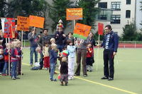 Mit Plakaten und Trillerpfeifen demonstrieren Eltern und Kinder auf dem Platz an der Körtestraße, im Hintergrund die Wohnhäuser.