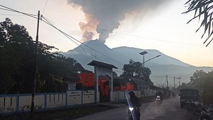 Menschen fahren Motorrad in Flores Timur, während aus dem Vulkan heißer Dampf aufsteigt. 
