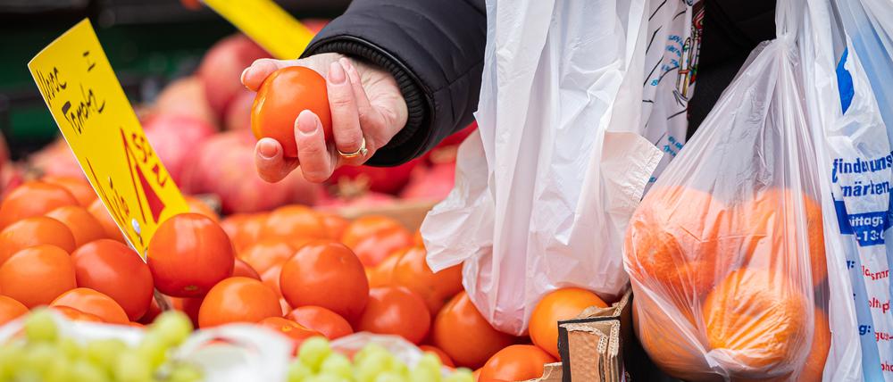 Eine Kundin begutachtet eine Tomate an einem Stand auf einem Wochenmarkt.