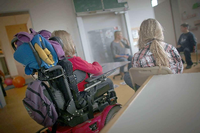 Eine Schülerin sitzt im Rollstuhl an einem Tisch im Klassenzimmer.