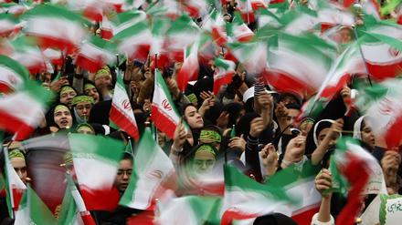 Iranische Flaggen werden während einer Demonstration in die Höhe gehalten.