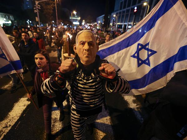 A left-wing Israeli protester wearing a mask depicting Prime Minister Benjamin Netanyahu attends a rally.