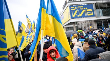 24.02.2023, Berlin: Teilnehmer einer Demonstration unter dem Motto «Wir werden nie vergessen» stehen an der Karl-Marx-Allee vor dem Cafe Moskau, das für ein paar Tage in Cafe Kyiv (Kiew) umbenannt wurde. 