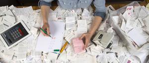Eine junge Frau sortiert am Schreibtisch, diverse Belege, Unterlagen, Rechnungen und Kassenbons für die Steuererklärung.
