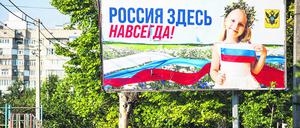 Eine Frau in Cherson geht an einem Plakat vorbei, auf dem „Russland ist für immer hier“ steht.