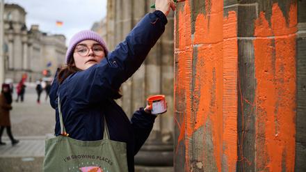 16.11.2023, Berlin: Eine Klimaaktivistin bemalt das Brandenburger Tor mit oranger Farbe. Die Gruppe Letzte Generation teilte am Donnerstag mit, dass Mitglieder mit Pinseln die Westseite des Bauwerks eingefärbt haben. Die Polizei Berlin berichtete, dass zwei Klimaaktivisten festgenommen wurden. Foto: Annette Riedl/dpa +++ dpa-Bildfunk +++