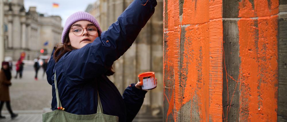 Eine Klimaaktivistin bemalt das Brandenburger Tor mit oranger Farbe.