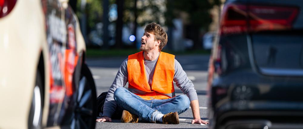 Ein Klimaaktivist sitzt am Karlsplatz in der Münchner Innenstadt auf der Fahrbahn und blockiert die Straße.