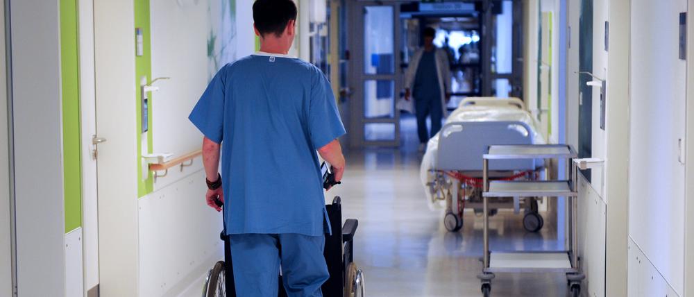 Ein Pfleger schiebt einen Rollstuhl über einen Flur in einem Krankenhaus. 