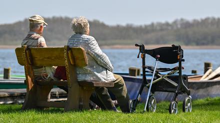 Ein älteres Paar sitzt auf einer Bank am Ufer eines Sees und genießt das sonnige Frühlingswetter. 