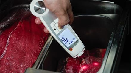 Ein Lebensmittelkontrolleur hält in der Küche eines Restaurants ein Thermometer an Fleischstücke. 