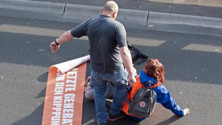 Bei einer Blockade der Gruppe Letzte Generation auf der Stadtautobahn unweit des Kurfürstendamms tritt ein Mann gegen einen Aktivisten.