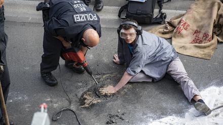 Wenn die Polizei zur Hilti greifen muss: Ein Polizei stemmt Asphalt aus der Straße, an den sich ein Aktivist geklebt hat.