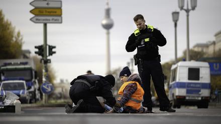 Polizisten lösen eine Aktivistin der Gruppe „Letzte Generation“ von der Kreuzung Frankfurter Tor, die sich bei einer Sitzblockade mit einer Hand am Asphalt festgeklebt hat.