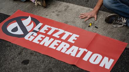 Ein Aktivist der Gruppe „Letzte Generation“, der seine Hand auf der Straße festgeklebt hat, blockiert eine Kreuzung. 