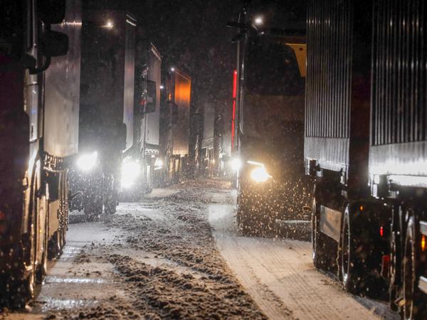 Lastkraftwagen stauen sich auf der Autobahn A5 bei Grünberg auf schneebedeckter Fahrbahn.