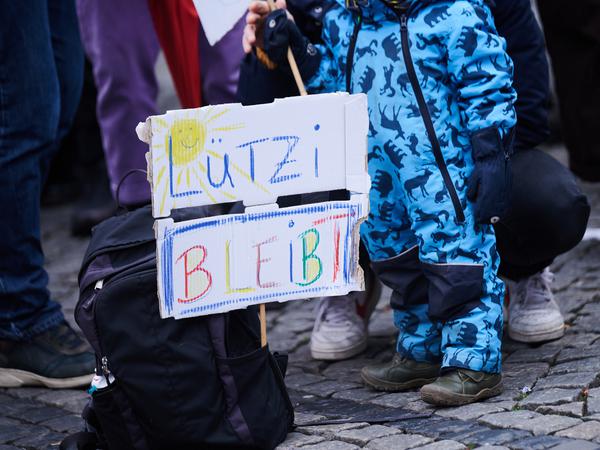 „Lützi bleibt“ steht auf einem Plakat, das vor einem Kind in einem Rucksack steckt. Über 300 Personen nehmen an der Demonstration gegen die Räumung Lützeraths auf dem Hermannplatz teil.