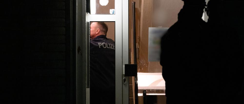 Polizisten stehen im Hausflur eines Mehrfamilienhauses und vor der Eingangstür. Bei einem Polizeieinsatz im brandenburgischen Senftenberg war hier in der vorletzten Woche ein Mann durch Schüsse von Beamten tödlich verletzt worden. Er soll sie mit einem „axtähnlichen Gegenstand“ angegriffen haben. Die Ermittlungen laufen.  