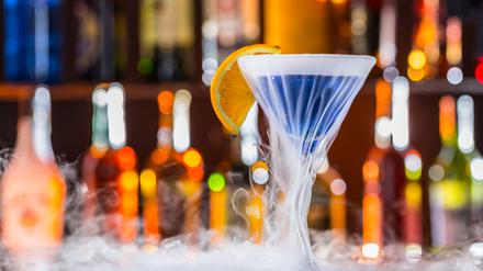 Ein blauer Cocktail in einem Martiniglas steht auf einem Tresen.