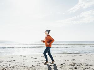 Eine junge Frau joggt barfuß am Strand entlang.