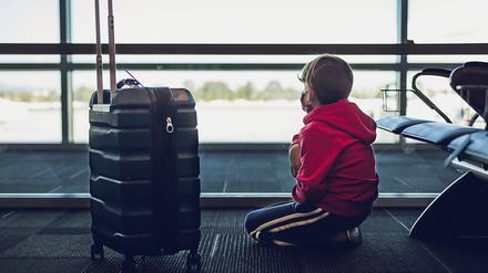 Young Boy Next To Suitcase Looking Out The Window At Airport.