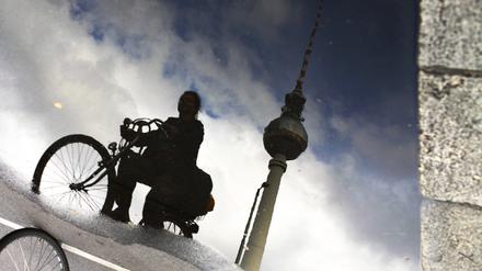 Radfahrerin spiegelt sich in Pfütze mit Fernsehturm am Alexanderplatz in Berlin.