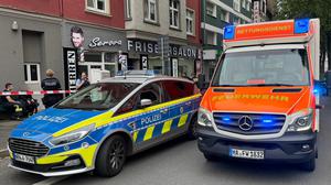 Ein Einsatzfahrzeug der Polizei und ein Rettungswagen der Feuerwehr stehen vor einem Friseursalon. In Hagen sind am Samstagmittag an zwei Orten mehrere Schüsse gefallen und mehrere Personen verletzt worden. 