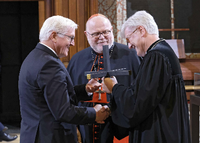 Landesbischof Bedford-Strohm (r.) und Kardinal Marx überreichen ein Kreuz an Bundespräsident Steinmeier (l.)