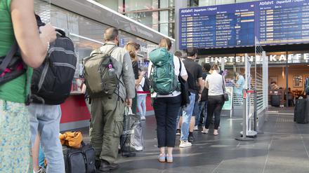  Reisende stehen im Berliner Hauptbahnhof am DB-Infoschalter.