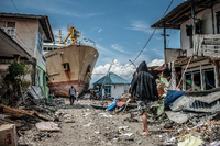 Indonesien, Palu: Menschen gehen eine Straße entlang in der Nähe des Ortes, wo ein Schiff während des Tsunamis an Land gespült wurde. Rund 5000 Menschen werden nach den Erdbeben und dem Tsunami in Indonesien noch immer vermisst.