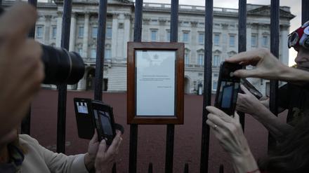 Menschen fotografieren die Bekanntgabe des Todes von Königin Elizabeth II., die an den Toren des Buckingham Palace hängt. 