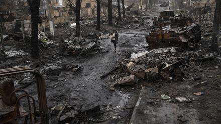 Ukraine, Butscha: Eine Frau geht auf einer Straße, die übersät ist mit zerstörten russischen Militärfahrzeugen.