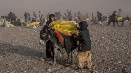 12.10.2023, Afghanistan, Herat: Afghanen erhalten Hilfsgüter, während im Dorf Chahak nach einem Erdbeben im Bezirk Zenda Jan in der Provinz Herat im Westen Afghanistans ein Sandsturm wütet. 
