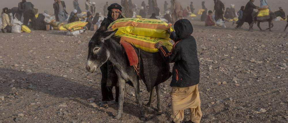 12.10.2023, Afghanistan, Herat: Afghanen erhalten Hilfsgüter, während im Dorf Chahak nach einem Erdbeben im Bezirk Zenda Jan in der Provinz Herat im Westen Afghanistans ein Sandsturm wütet. 