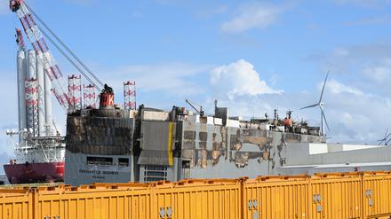 Der schwer beschädigte Autofrachter »Fremantle Highway« liegt im Hafen, abgeschirmt durch gelbe Container. 