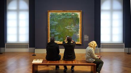 Besucher sitzen im Museum Barberini vor dem Bild „Seerosen“ (1914 bis 1917) von Claude Monet auf einer Bank.