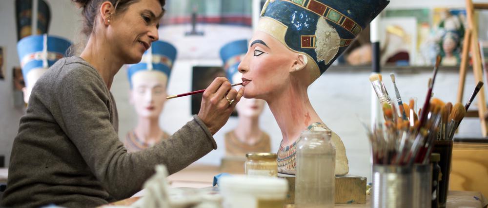 Eine Skulpturenmalerin arbeitet in der Gipsformerei an einer Nachbildung des Nofretete-Kopfes.