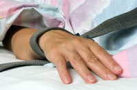 Eine mit einem Textilband festgebundene Hand eines Patienten.